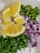 Sliced yellow lemons, chopped green chili peppers, diced red onions, and finely chopped fresh cilantro arranged on a white surface.