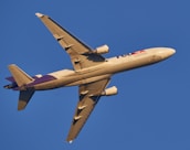 A commercial cargo airplane in flight against a clear blue sky. The aircraft is viewed from below and is painted in light colors with purple accents.