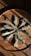 Herbs bundled with different colored strings are arranged in a circular pattern on a rustic wooden surface, casting shadows that enhance the texture of the wood.