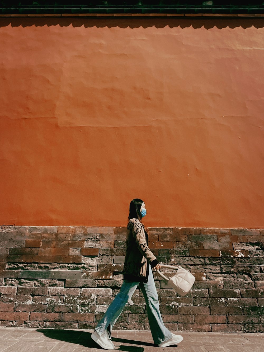 woman in black jacket and green pants standing on gray concrete brick wall during daytime