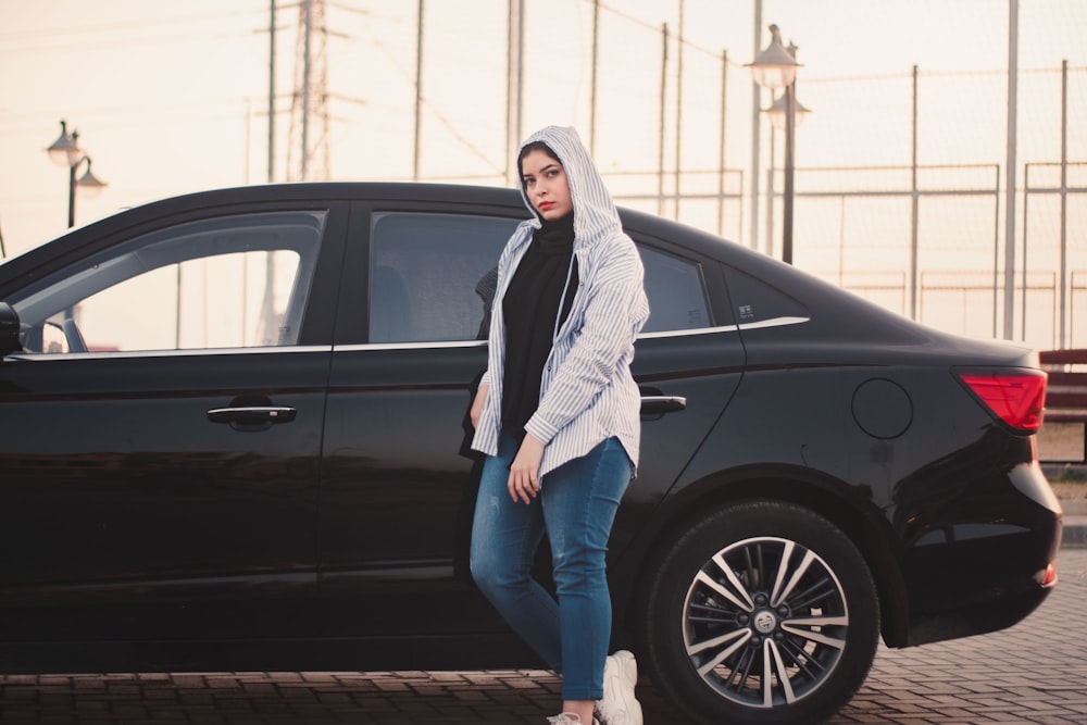 woman in white scarf and blue denim jeans standing beside black suv
