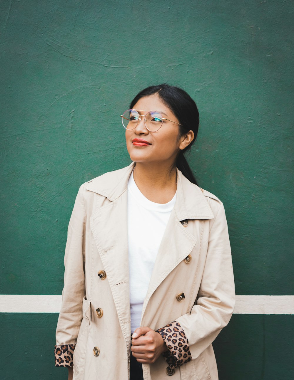 woman in beige coat standing near green wall