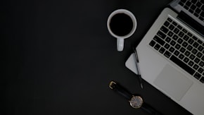 A sleek black and white photo of a minimalist desk with a laptop and a coffee cup, reflecting a professional yet smooth vibe.