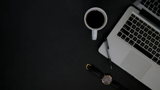 A professional office setting with a businessperson typing on a laptop, surrounded by notes and a cup of coffee.