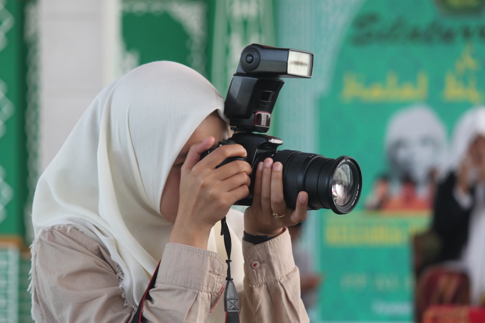 pessoa em hijab branco segurando câmera dslr preta