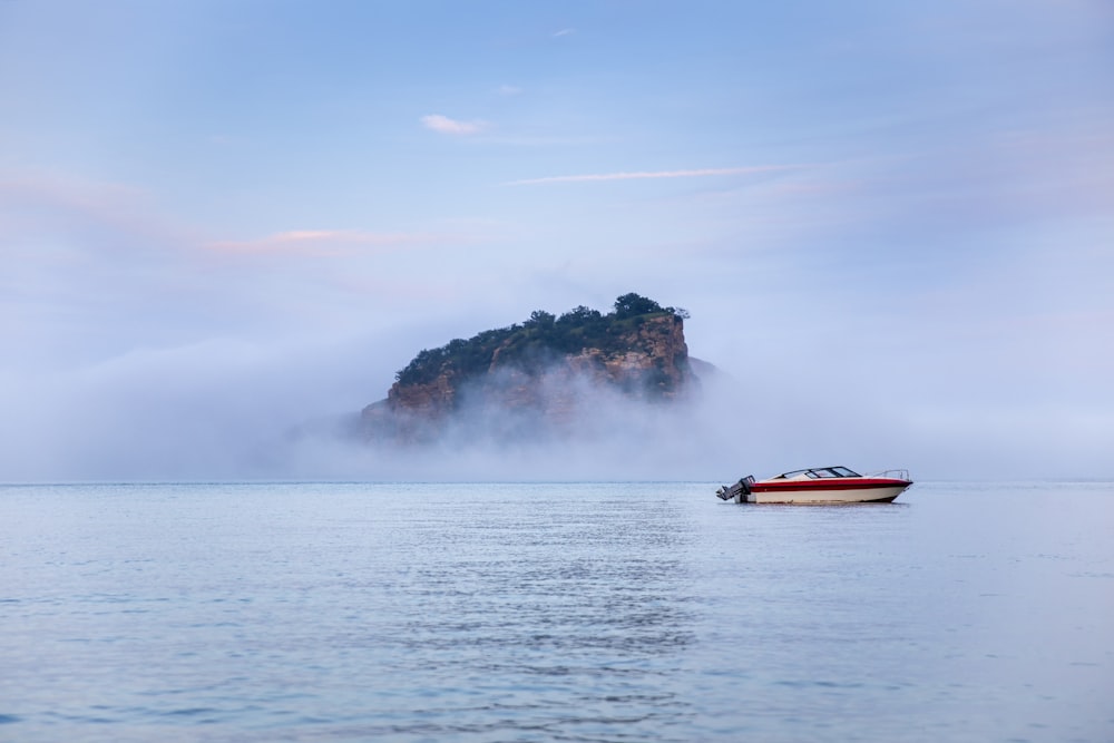 昼間は青空の下、緑と茶色の島の近くの海に浮かぶ赤と白のボート