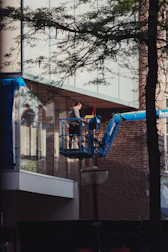 Certified caces technician on a lift in front of a large glass facade.