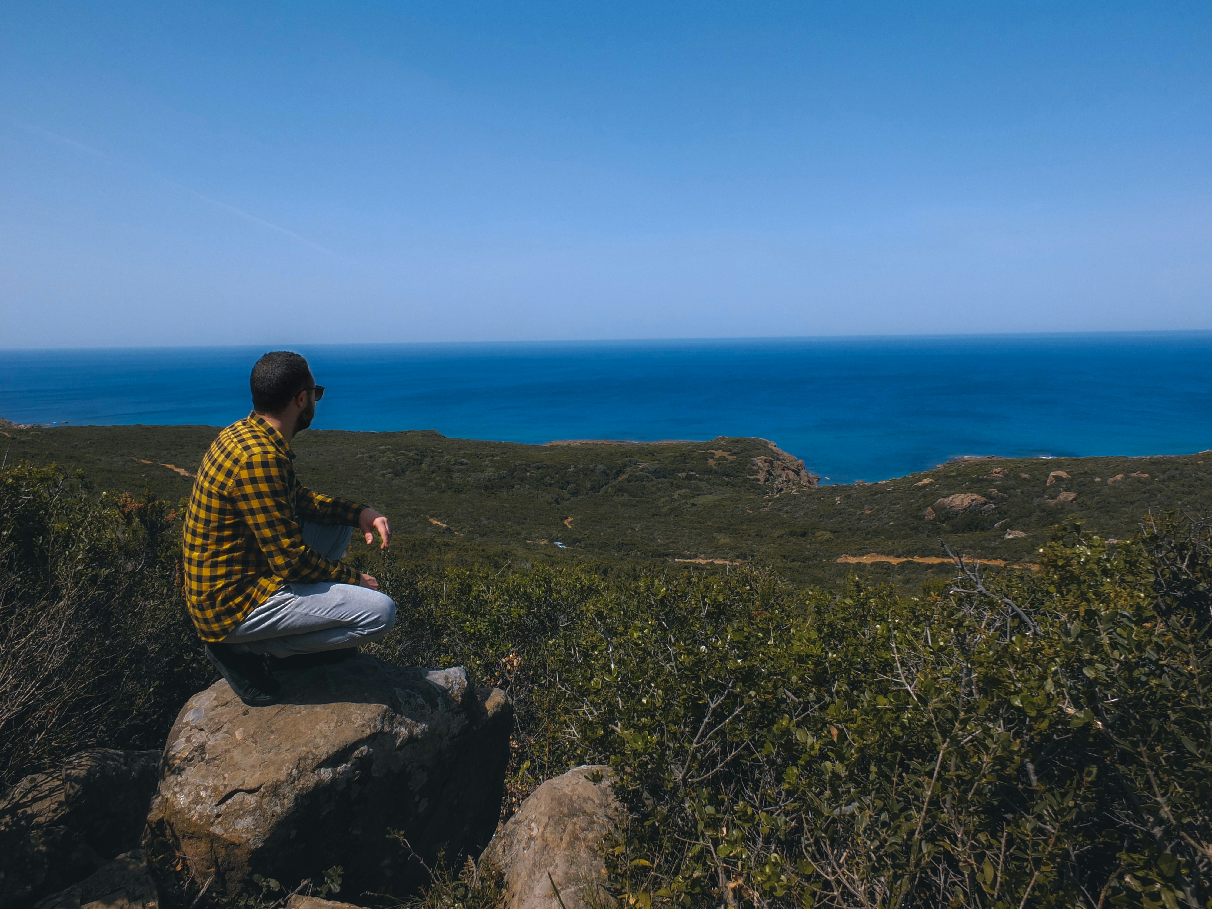 woman in yellow and black checkered dress shirt sitting on rock formation during daytime