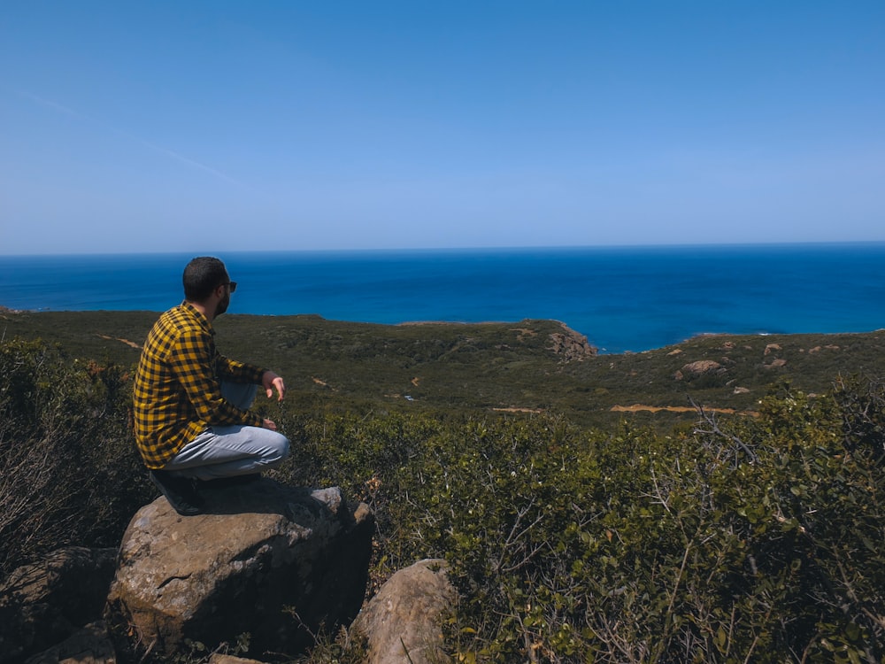 woman in yellow and black checkered dress shirt sitting on rock formation during daytime