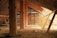 An old, rustic attic with wooden beams and walls, filled with scattered debris and straw on the floor. Light filters in through gaps in the wall slats, casting shadows and highlighting the textures of the wooden surfaces.