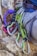 Several climbing carabiners in silver and green are attached to a harness on a person's waist, with a purple climbing rope lying nearby on a rock surface.
