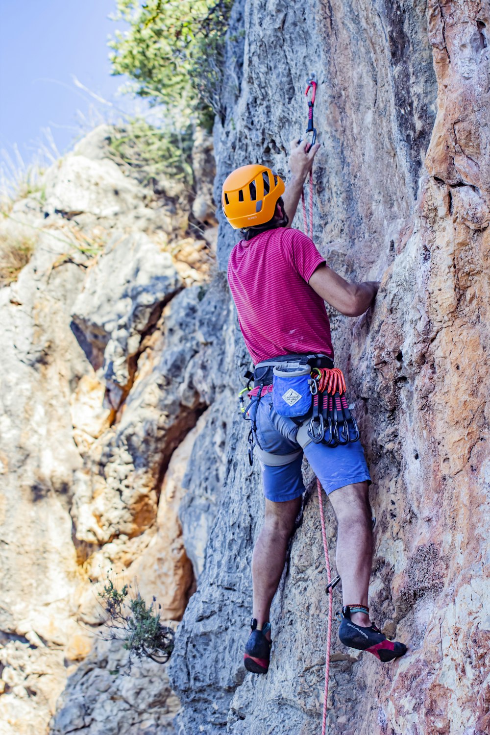 man in red t-shirt climbing on brown rock during daytime