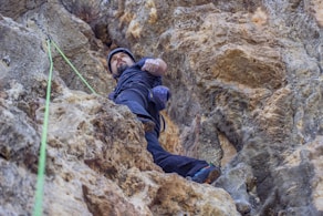 person in blue jacket climbing on brown rock mountain during daytime