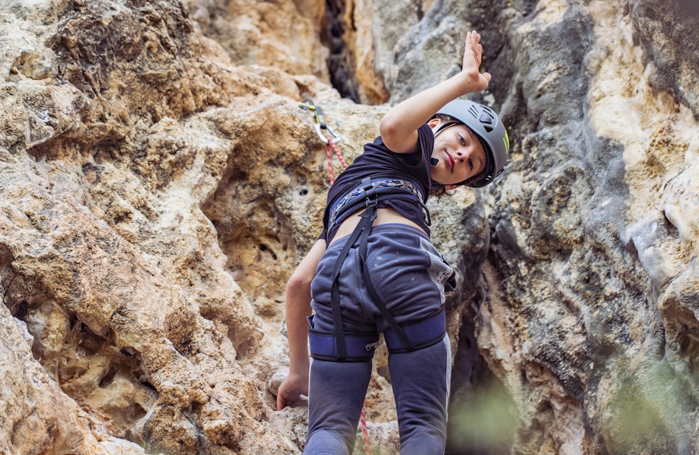 man in black t-shirt and blue denim jeans climbing on brown rock