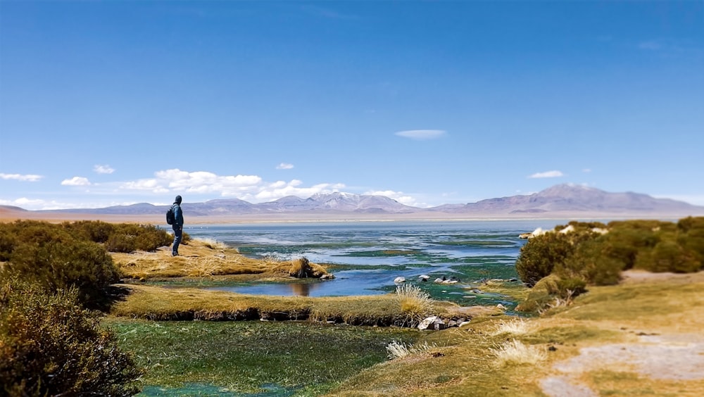 man in black jacket standing on green grass field near body of water during daytime