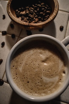 Close-up of steaming organic coffee in a rustic ceramic cup on a wooden table surrounded by fresh green tea leaves.