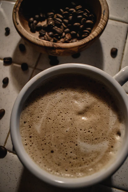 Close-up of a steaming cup of dark roasted coffee on a wooden table with coffee beans scattered around.