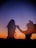 Silhouetted figures dance joyfully against a vivid sunset, with the sky transitioning from deep orange to dark blue. The motion conveys a sense of freedom and spontaneity.