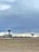 Two large satellite dishes are situated in an open, barren field with a few scattered trees in the distance. The sky above is cloudy, with a mix of grey and blue hues.