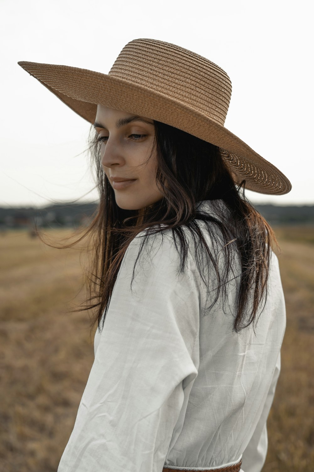 mulher na camisa branca da manga comprida que veste o chapéu de palha marrom