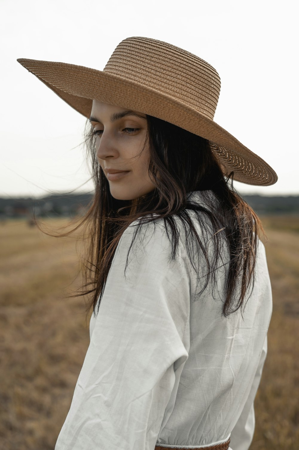 Femme en chemise blanche à manches longues portant un chapeau de paille marron