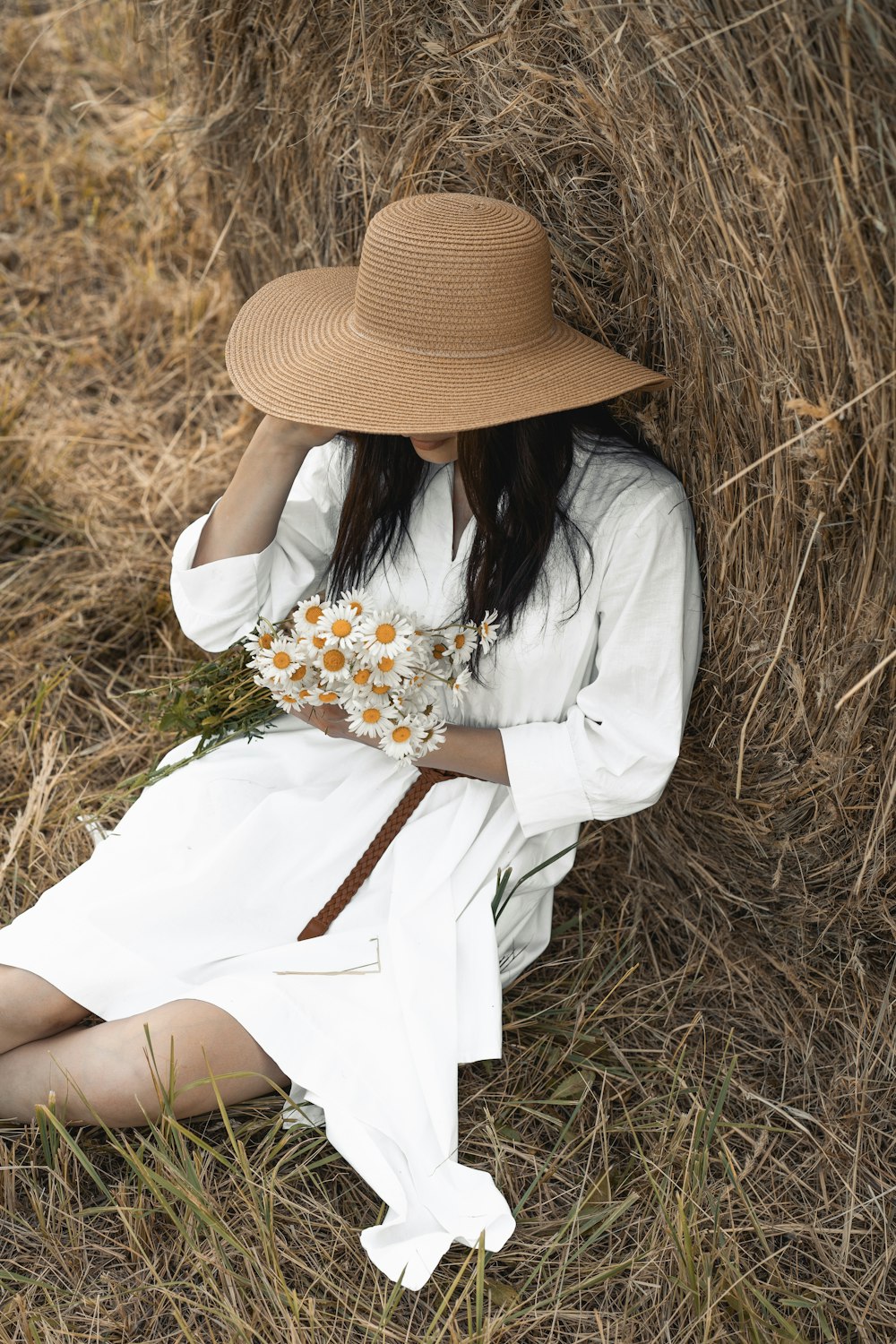woman in white long sleeve shirt and brown hat holding white and yellow flowers