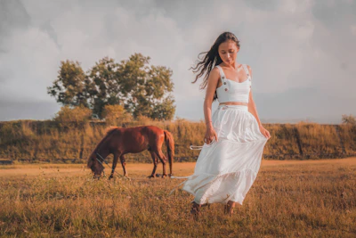 woman in white dress standing beside brown horse during daytime