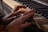 Hands are playing on a worn, possibly vintage piano keyboard. The keys appear to be aged and discolored, adding a sense of history and character.