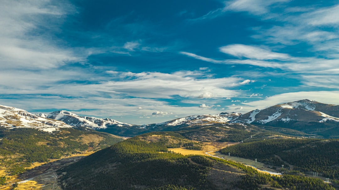 green and brown mountains under blue sky and white clouds during daytime, 4K Drone shot in High Quality as wallpaper or desktop image with a blue sky and green hillsides with snow-capped peaks.