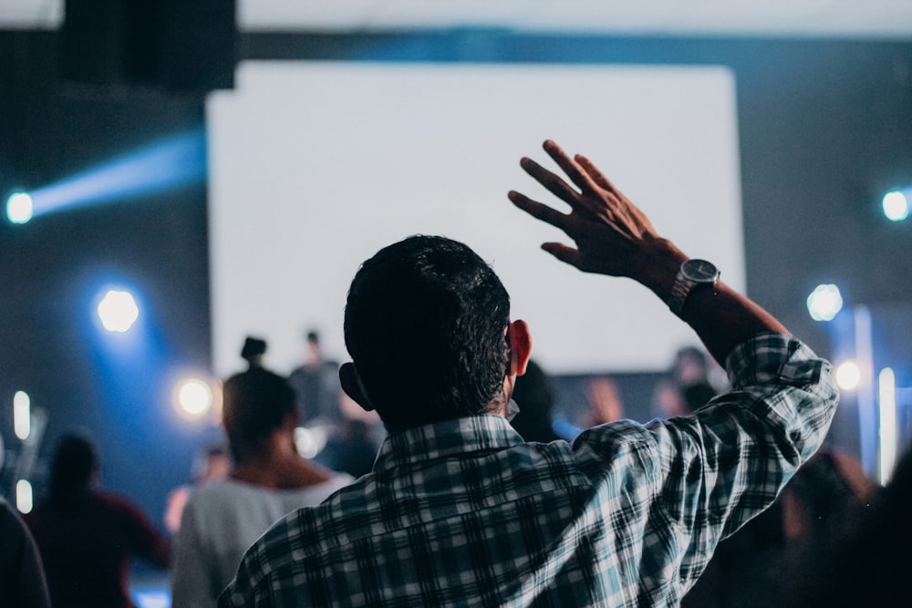 man in black and white plaid dress shirt raising his hands