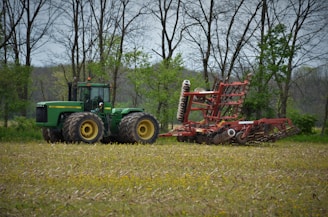 A green tractor parked in a sunny field ready for agricultural work.