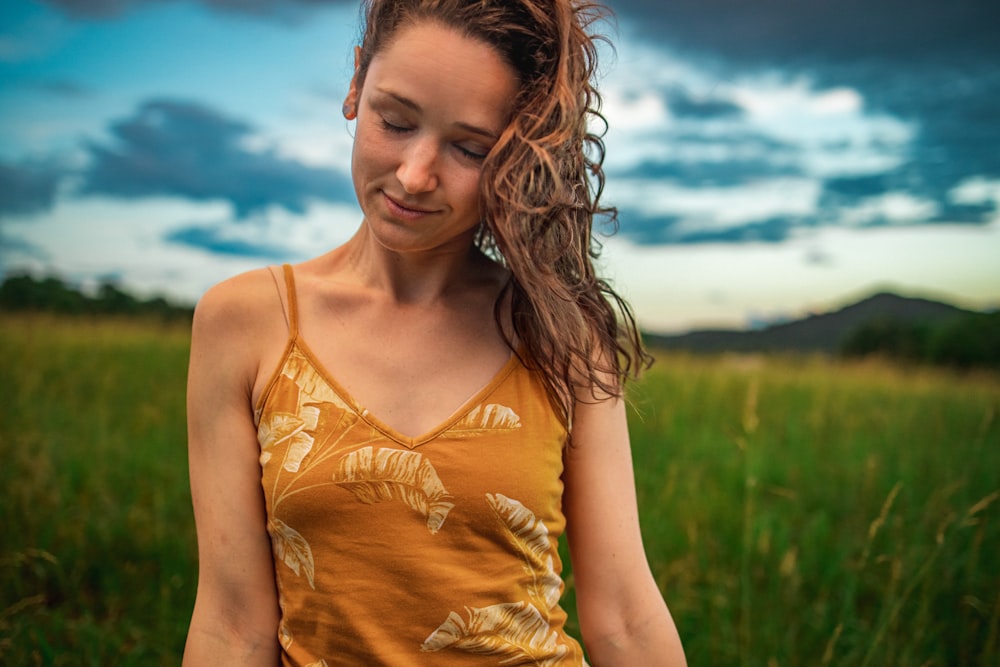 woman in yellow tank top standing on green grass field during daytime