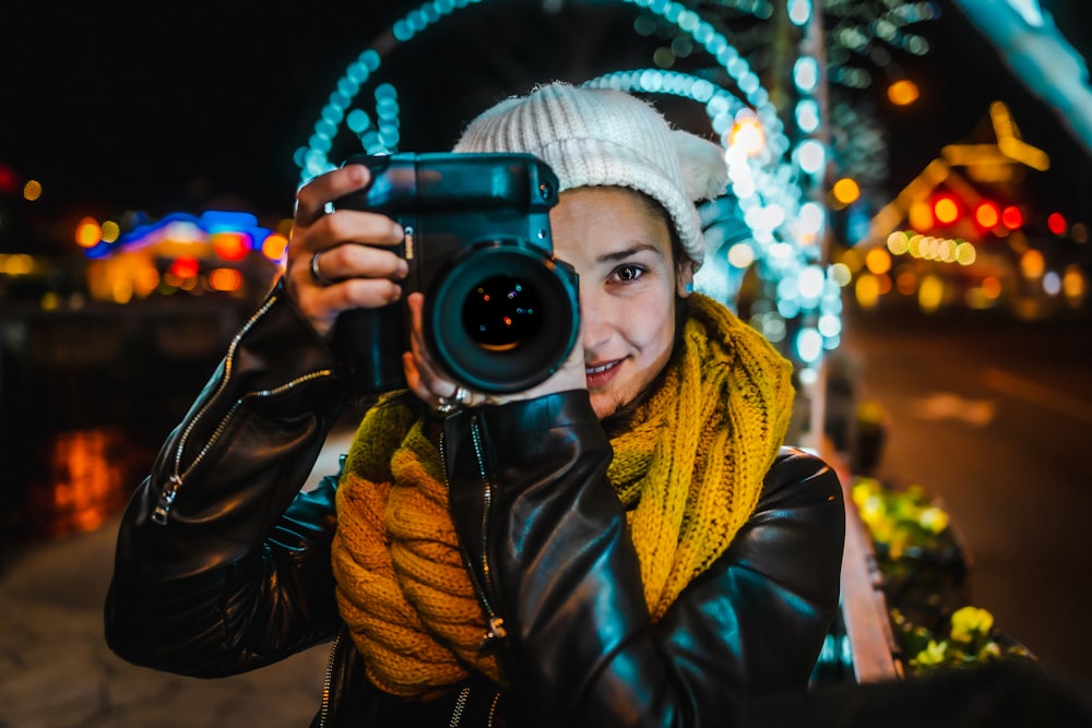 donna in giacca di pelle nera che tiene la macchina fotografica nera