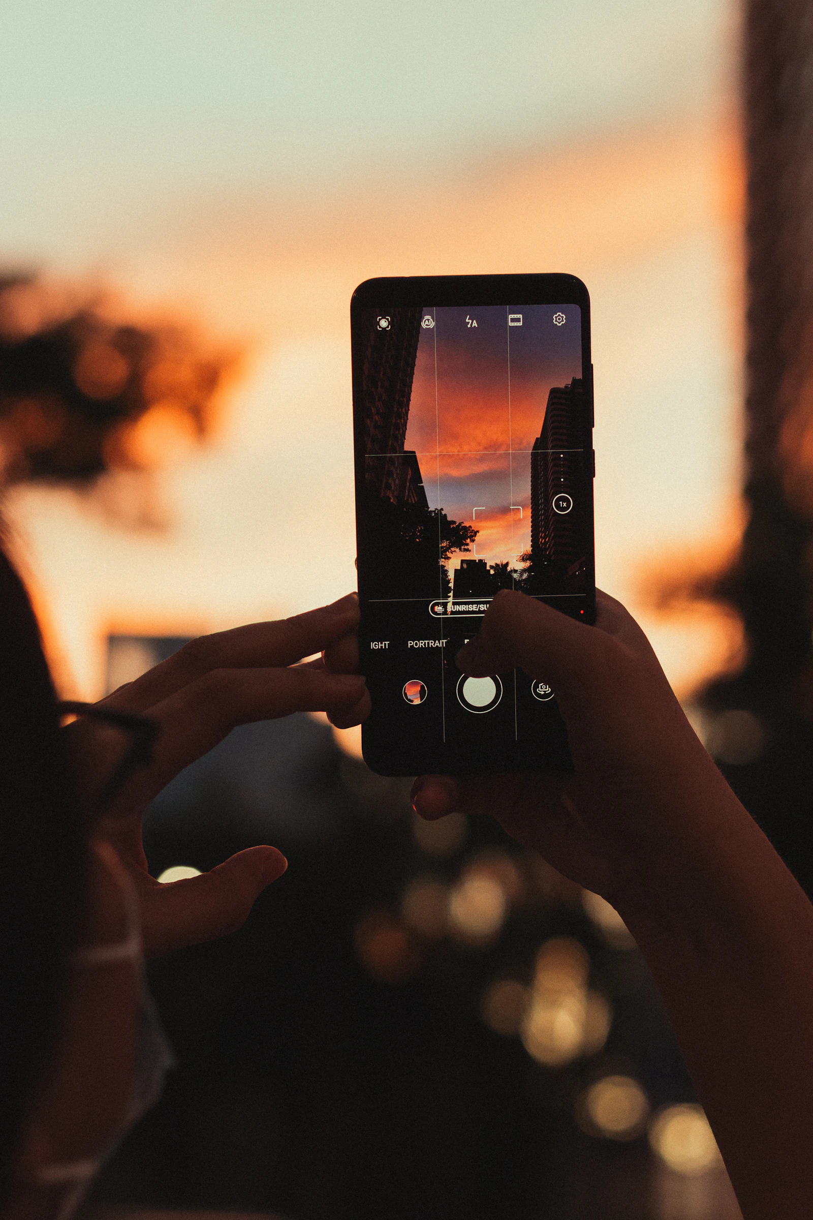 Smartphone camera screen framing an orange city sunset between tall buildings