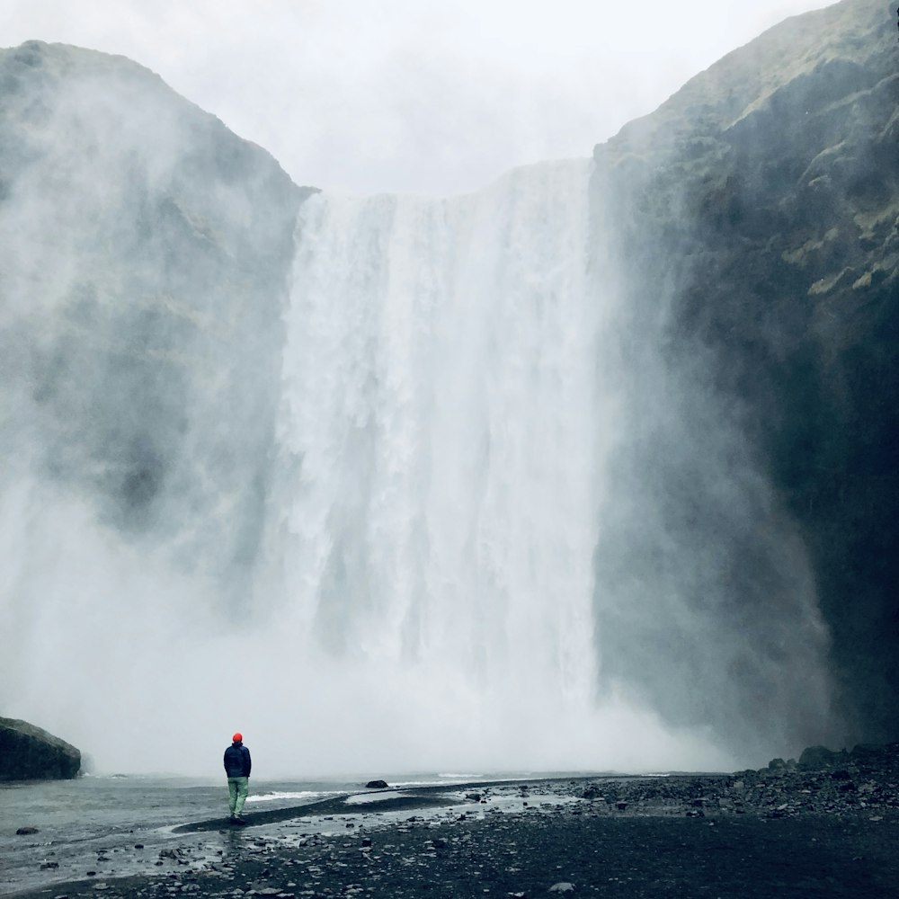 person in green jacket standing on gray concrete road near waterfalls during daytime