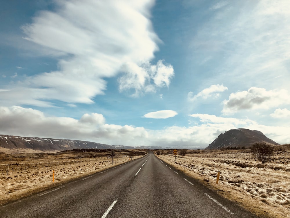 gray asphalt road under blue sky and white clouds during daytime