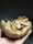 A hand holding a halved coconut shell filled with thinly sliced, toasted coconut chips. The shell is rough and textured, with fibers visible on the outside. The background is dark, enhancing the focus on the coconut.