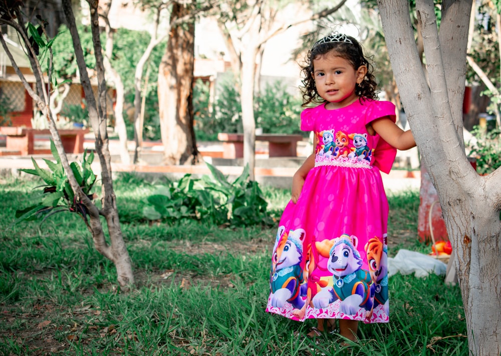 girl in pink and white floral dress standing on green grass field during daytime