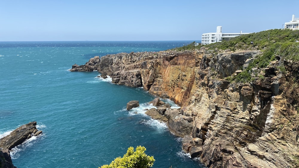 white and brown concrete building on brown rocky mountain beside blue sea during daytime