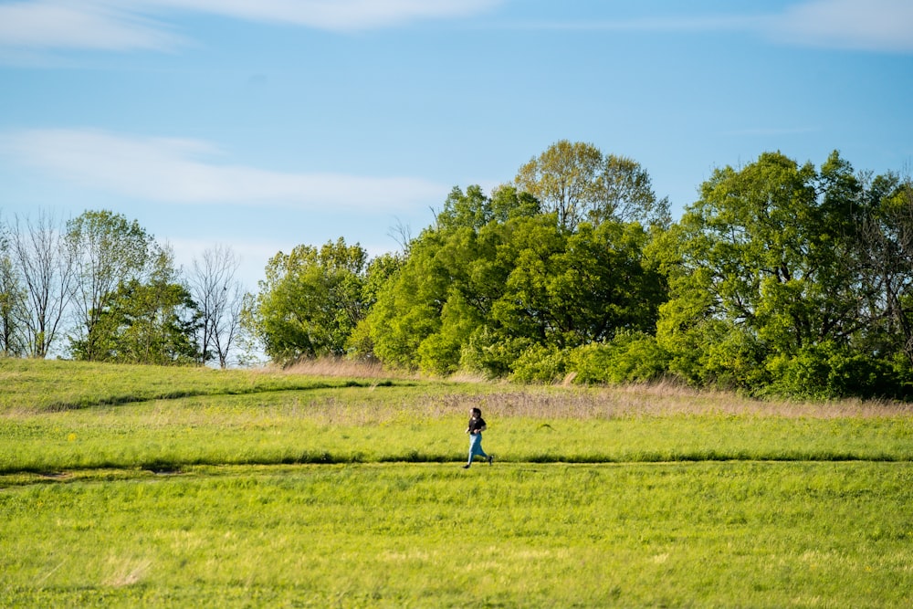 Hombre con camisa azul y pantalones negros caminando sobre el campo de hierba verde durante el día