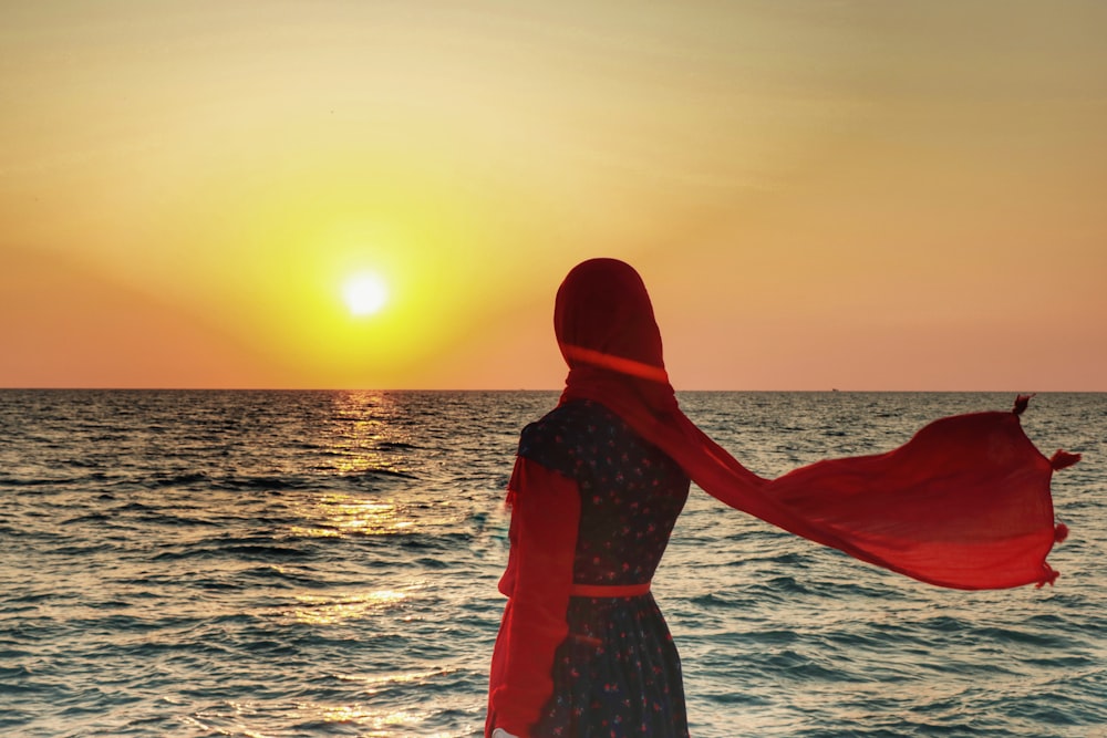 woman in red and white dress standing on sea shore during sunset