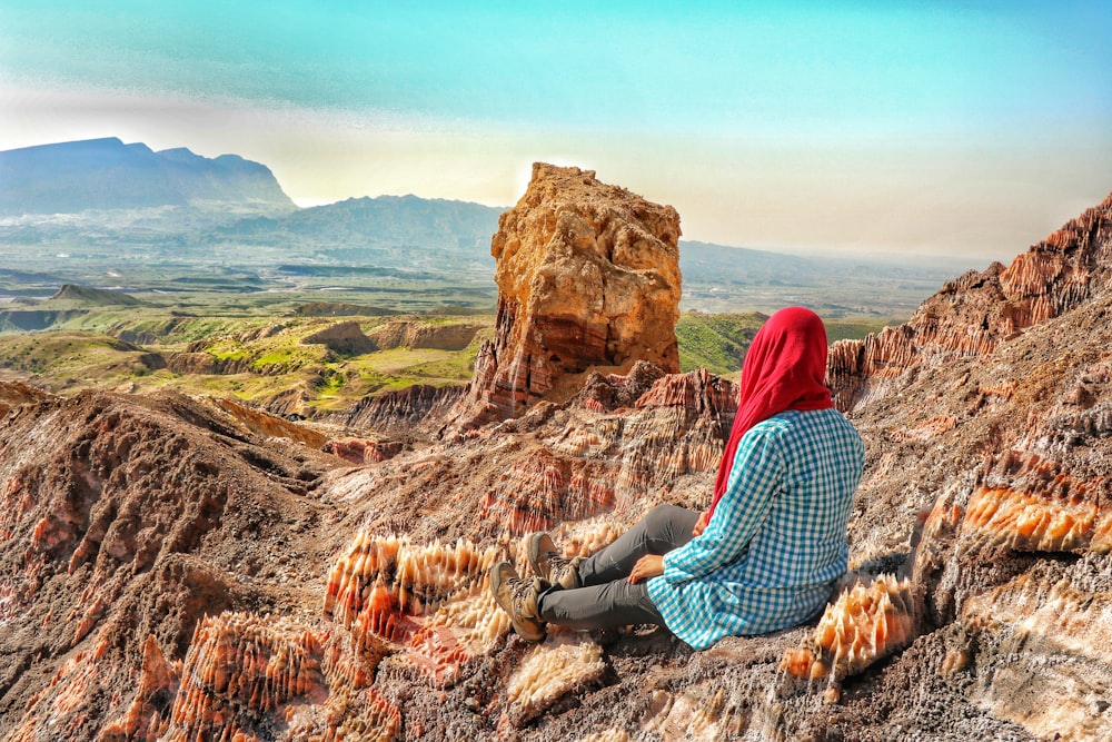 woman in red and white hijab sitting on brown rock formation during daytime