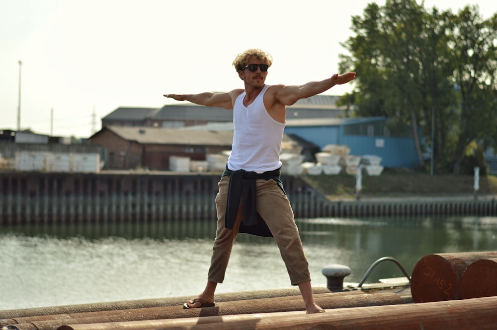 Hombre con camiseta blanca sin mangas y pantalones marrones saltando en el muelle de madera marrón durante el día