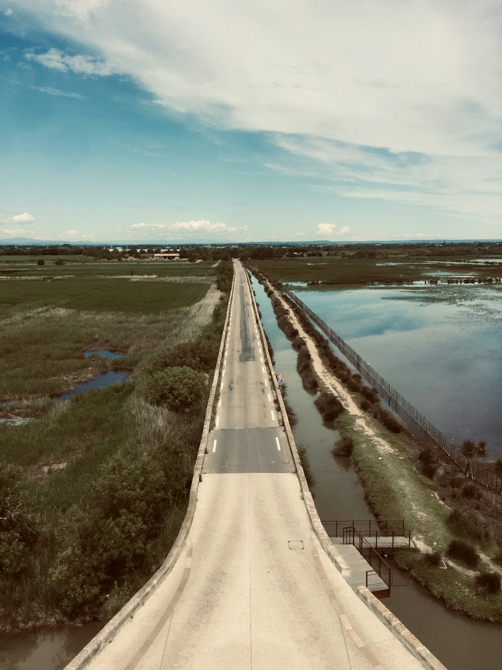 gray concrete road beside body of water under blue sky during daytime