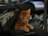 A ginger cat with one eye is reclining on a motorcycle seat. Its fur is a rich orange color, and the background shows parts of the motorcycle and some blurred urban elements.