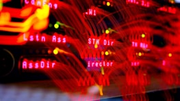 A close-up view of a server room or data center with bright red LED lights. The lights form various technical terms, suggesting network or server activity. The background is dark, highlighting the vibrant, dynamic lines and letters.