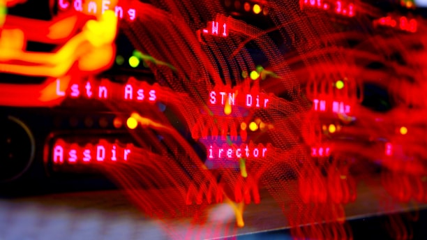 A close-up view of a server room or data center with bright red LED lights. The lights form various technical terms, suggesting network or server activity. The background is dark, highlighting the vibrant, dynamic lines and letters.