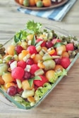 A colorful fruit salad in a clear glass bowl with a sprinkle of mint.