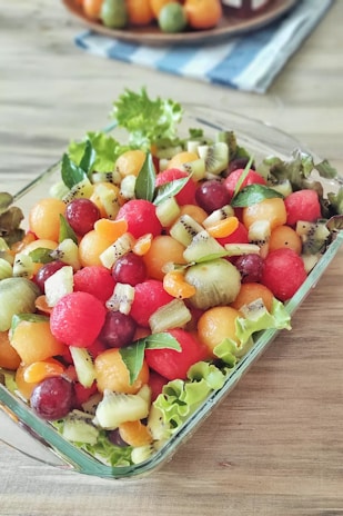 A colorful fruit salad sprinkled with bright fruit salad masala, served in a clear glass dish.