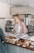 A joyful woman standing proudly in her cozy bakery surrounded by fresh bread and pastries.